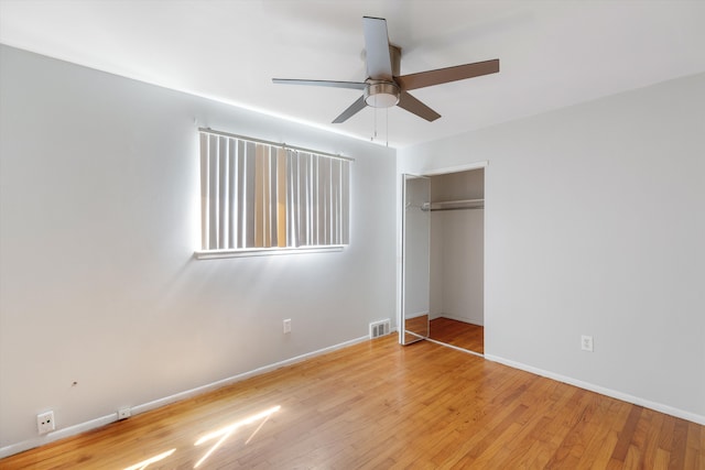 unfurnished bedroom featuring ceiling fan, visible vents, wood finished floors, baseboards, and a closet