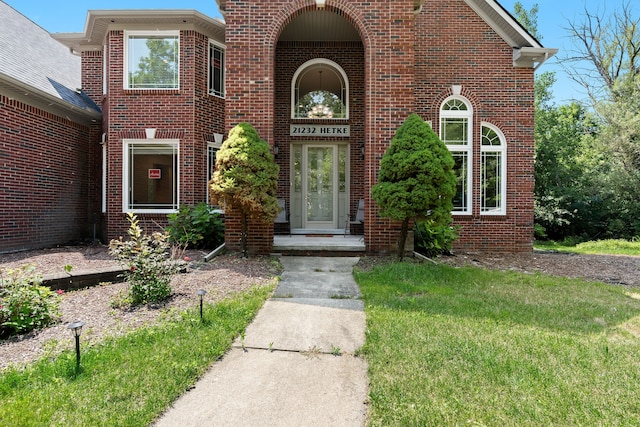 entrance to property featuring a lawn and brick siding