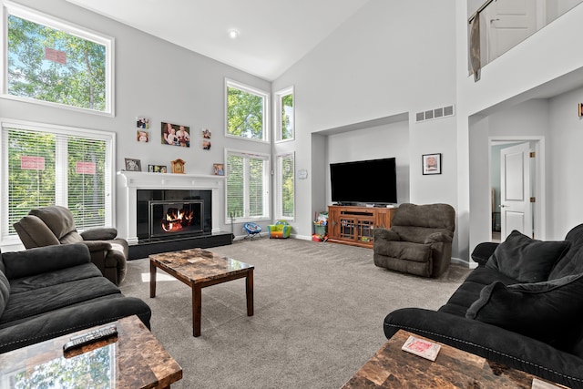carpeted living room featuring baseboards, a glass covered fireplace, visible vents, and high vaulted ceiling