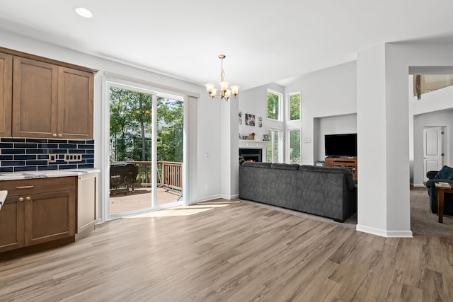 unfurnished living room featuring an inviting chandelier, a healthy amount of sunlight, light wood-style flooring, and baseboards