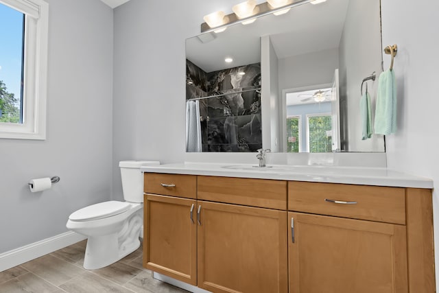 bathroom with wood finished floors, vanity, baseboards, a tile shower, and toilet