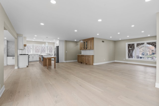 unfurnished living room with bar area, light wood finished floors, baseboards, visible vents, and recessed lighting