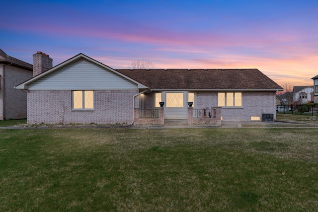 rear view of house with brick siding, a yard, a shingled roof, and central AC unit