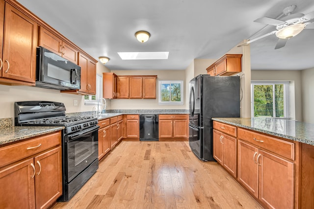 19737 Clement Rd, Northville, MI 48167 - kitchen with black appliances, a skylight, light wood-style floors, a sink, and stone countertops