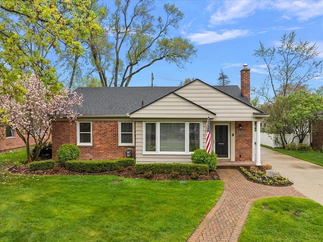 view of front facade with brick siding, a shingled roof, a front lawn, and a chimney