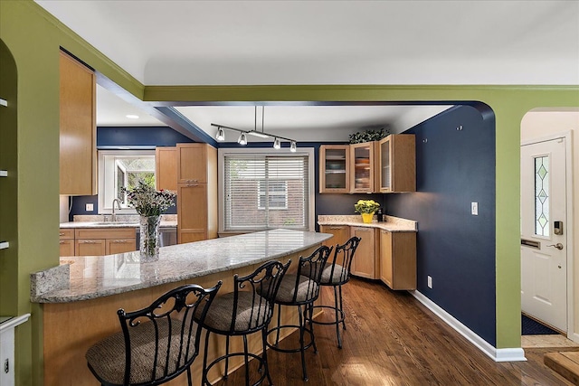 kitchen with dark wood-style flooring, light stone countertops, glass insert cabinets, a kitchen breakfast bar, and a sink