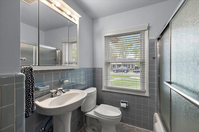bathroom featuring wainscoting, baseboard heating, toilet, enclosed tub / shower combo, and tile walls