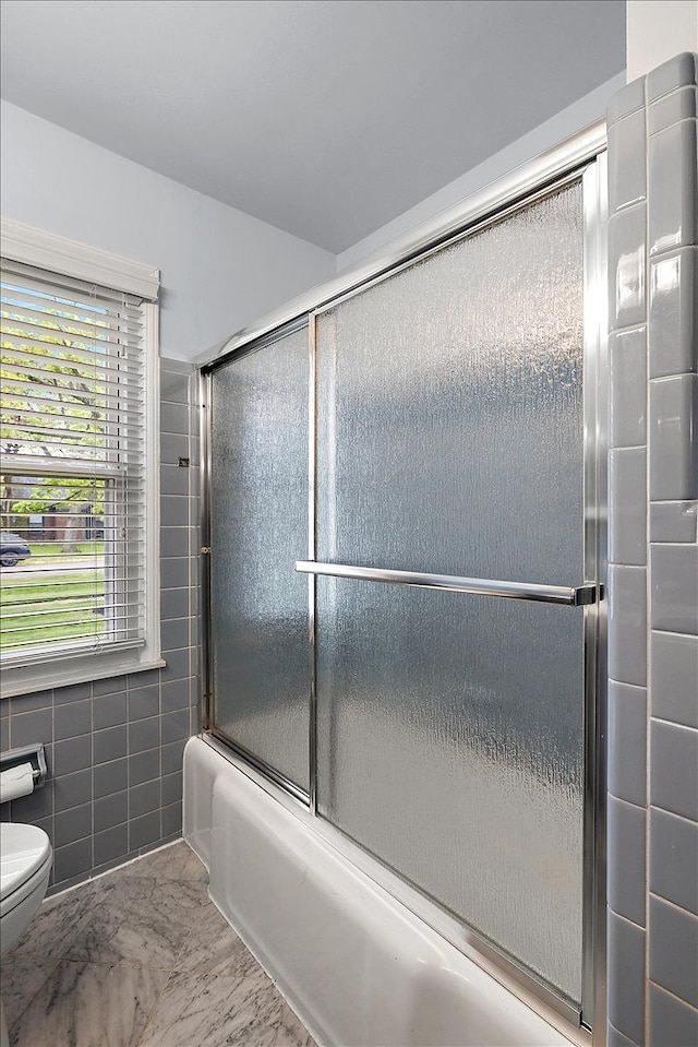 full bath with bath / shower combo with glass door, marble finish floor, toilet, and tile walls