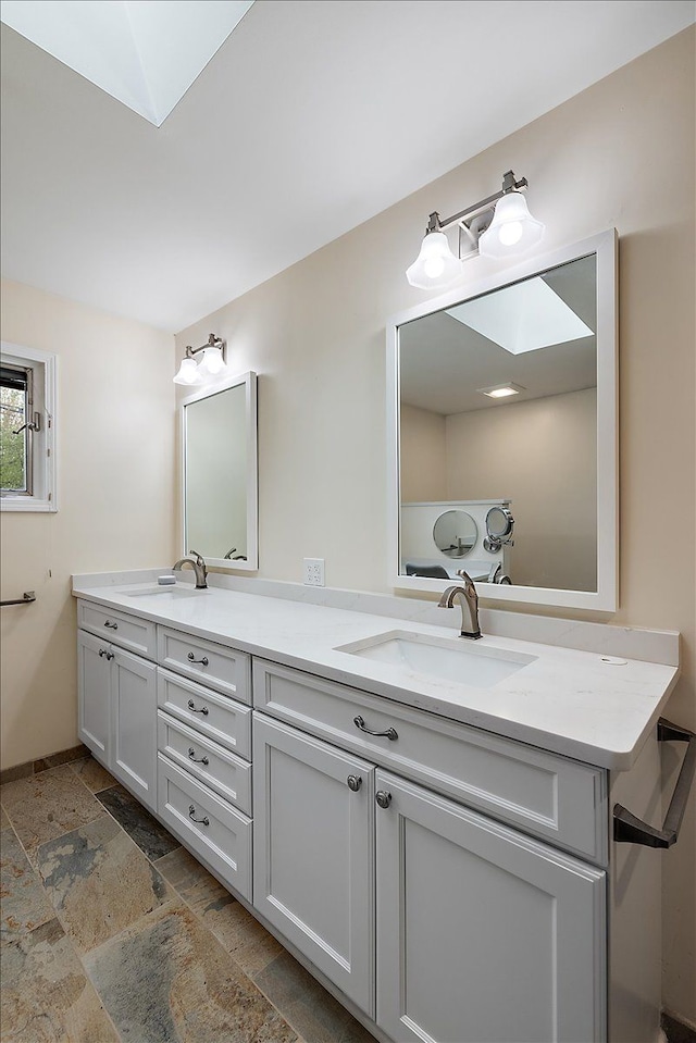 bathroom featuring stone tile floors, double vanity, a skylight, and a sink