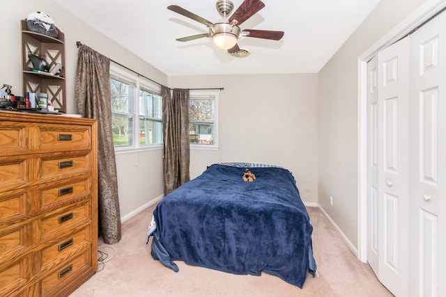 bedroom with light colored carpet, ceiling fan, baseboards, and a closet