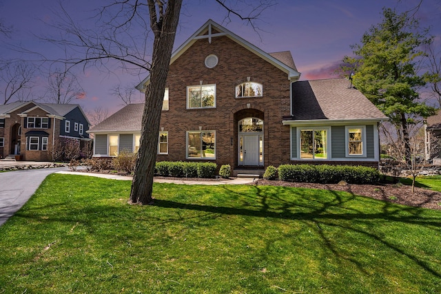 view of front of home featuring a shingled roof, brick siding, and a front yard