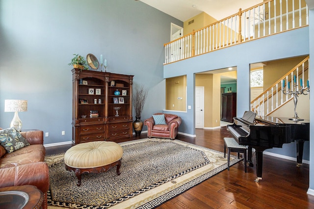 living area featuring baseboards, hardwood / wood-style flooring, a towering ceiling, and stairs