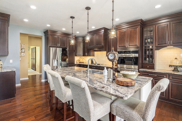 kitchen featuring a kitchen breakfast bar, dark wood finished floors, a sink, baseboards, and double oven