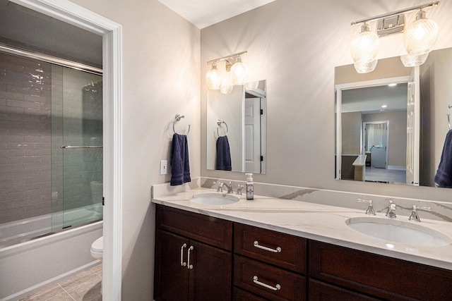 bathroom featuring double vanity, a sink, combined bath / shower with glass door, and toilet