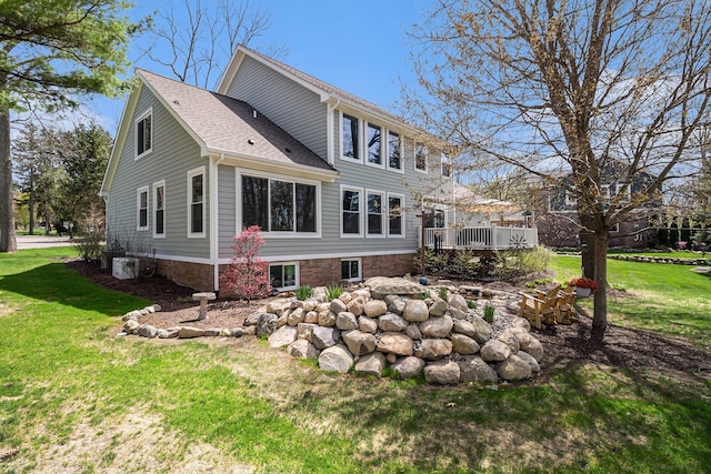 back of property with a lawn, a deck, central AC unit, and roof with shingles