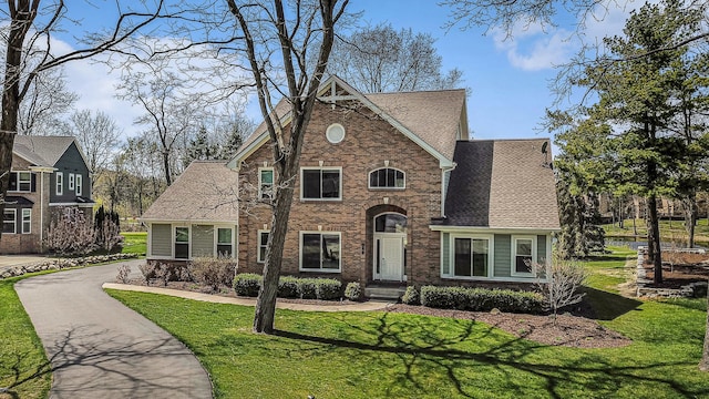 view of front of property featuring a shingled roof, a front lawn, and brick siding