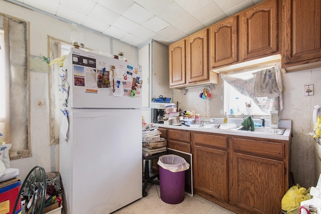 kitchen featuring brown cabinets, a sink, light countertops, and freestanding refrigerator