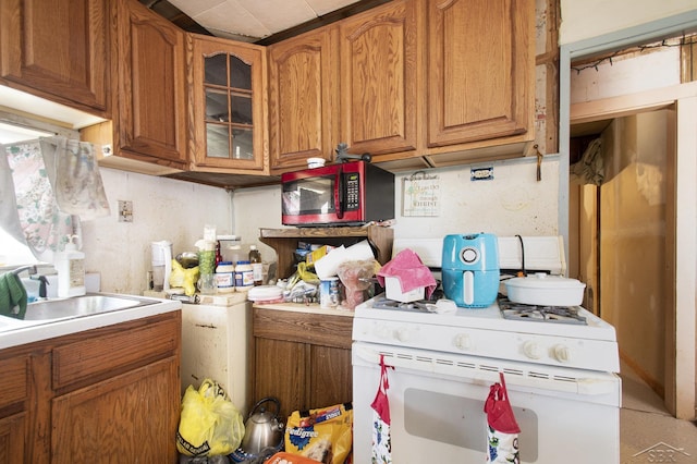 kitchen with white range with gas cooktop, glass insert cabinets, light countertops, and brown cabinets