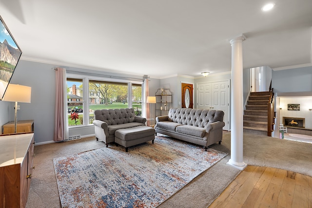 living area with ornamental molding, stairs, a warm lit fireplace, ornate columns, and light wood-type flooring