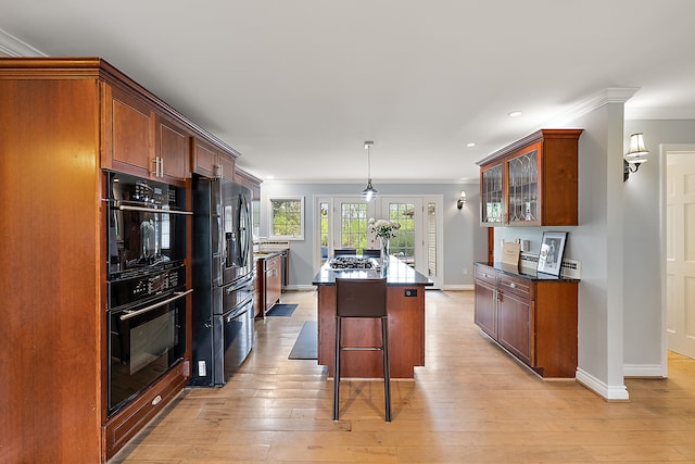 kitchen featuring crown molding, a center island, baseboards, black appliances, and light wood finished floors