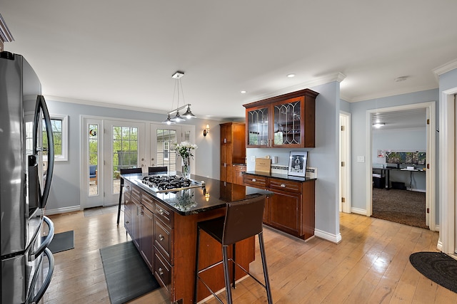 kitchen with stainless steel gas cooktop, baseboards, glass insert cabinets, ornamental molding, and black fridge