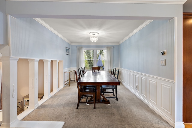 carpeted dining space with crown molding, a chandelier, wainscoting, and a decorative wall