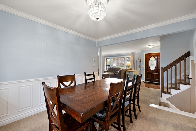 carpeted dining space with crown molding, an inviting chandelier, stairs, and a wainscoted wall