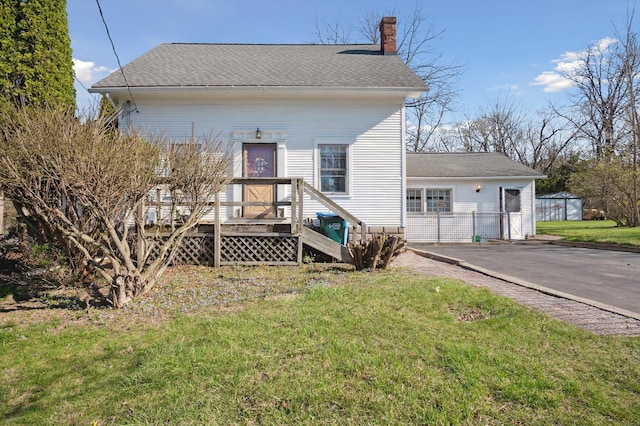 rear view of property featuring a lawn, driveway, a chimney, and a shingled roof