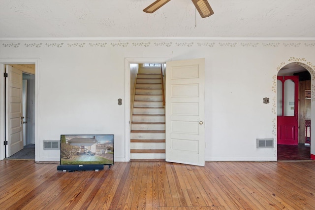 living area featuring a ceiling fan, hardwood / wood-style floors, stairs, arched walkways, and visible vents