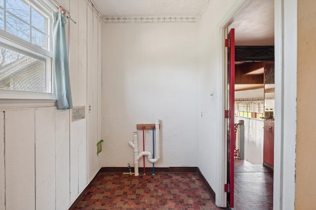 clothes washing area with wood walls, brick floor, and baseboards