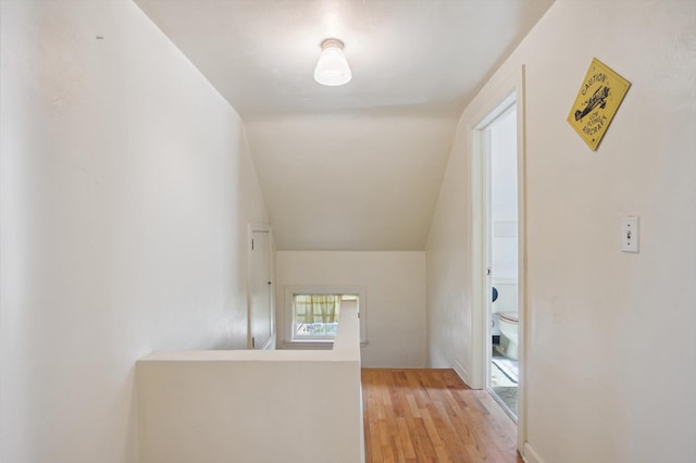 hallway featuring lofted ceiling, light wood-style flooring, and an upstairs landing