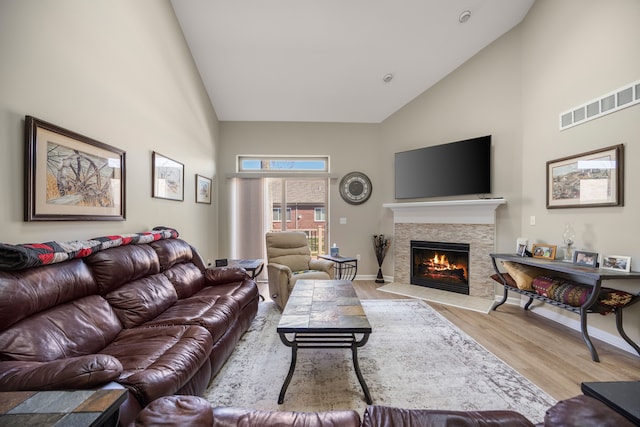 living area with a stone fireplace, visible vents, wood finished floors, baseboards, and high vaulted ceiling