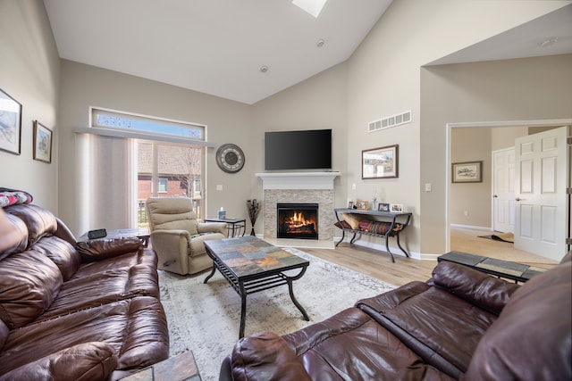 living area with high vaulted ceiling, wood finished floors, a stone fireplace, baseboards, and visible vents