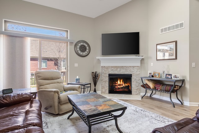 living room with a fireplace, wood finished floors, visible vents, and high vaulted ceiling