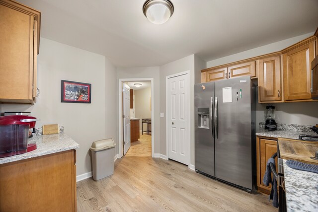 kitchen with light wood finished floors, baseboards, stainless steel fridge, and brown cabinets