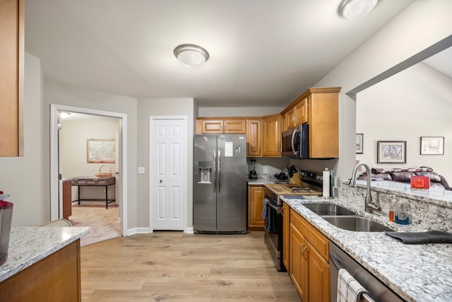 kitchen featuring light wood finished floors, a sink, light stone countertops, brown cabinetry, and appliances with stainless steel finishes