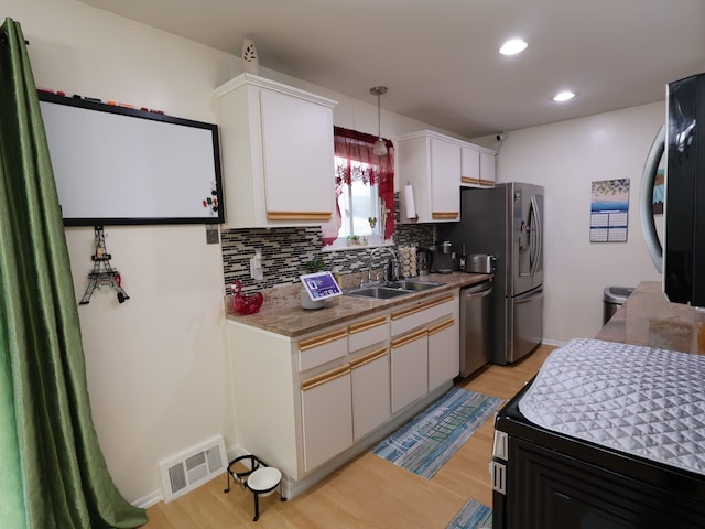 kitchen featuring visible vents, tasteful backsplash, a sink, light wood finished floors, and appliances with stainless steel finishes