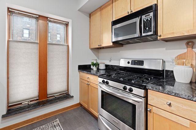 kitchen with light brown cabinetry, baseboards, appliances with stainless steel finishes, and dark stone counters