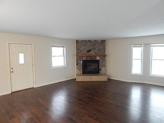 unfurnished living room with dark wood-type flooring, baseboards, and a stone fireplace