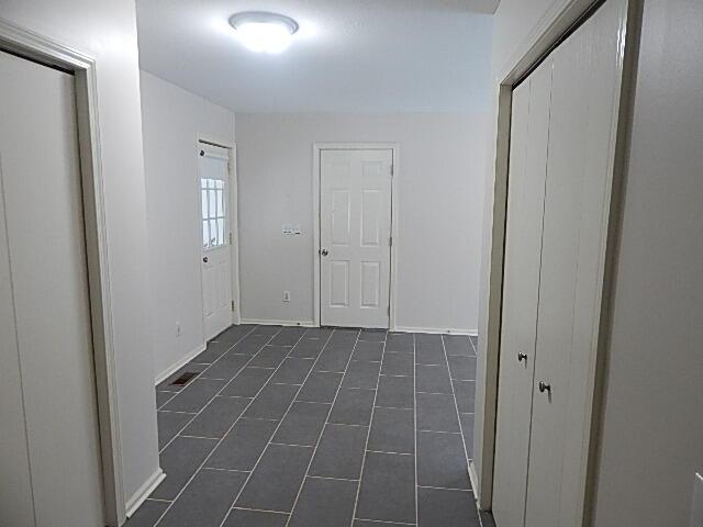 corridor featuring baseboards and dark tile patterned floors