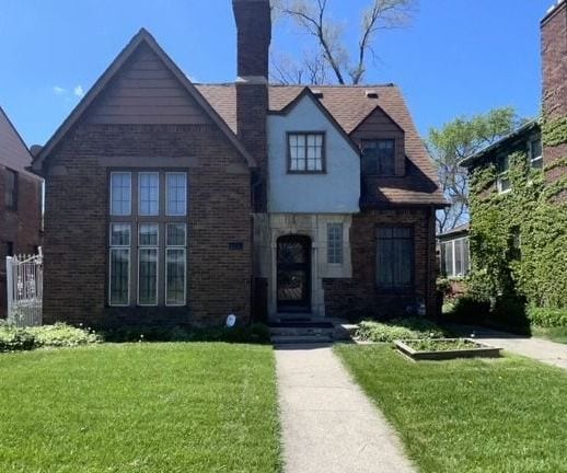 tudor home featuring stone siding, a chimney, and a front yard