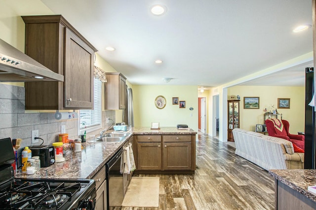 kitchen featuring backsplash, wood finished floors, wall chimney range hood, black appliances, and a peninsula