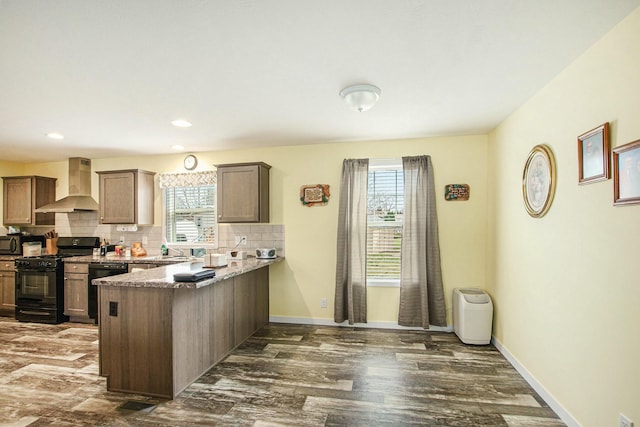 kitchen featuring a peninsula, wall chimney exhaust hood, a healthy amount of sunlight, and black appliances