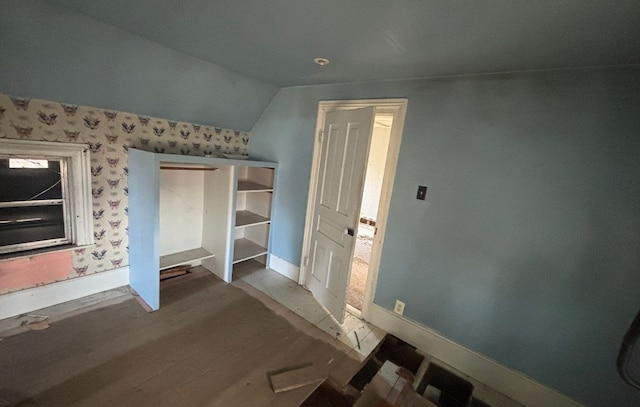 interior space with baseboards, wallpapered walls, wood finished floors, and vaulted ceiling