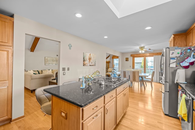 kitchen with ceiling fan, appliances with stainless steel finishes, a center island, dark stone countertops, and light wood-type flooring