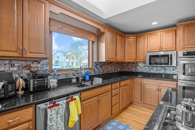 kitchen with stainless steel appliances, decorative backsplash, a sink, and dark stone countertops