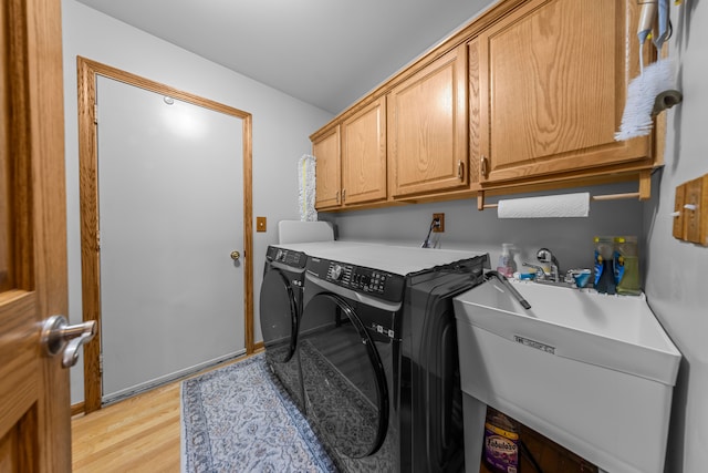 laundry room with a sink, light wood-type flooring, cabinet space, and washer and dryer