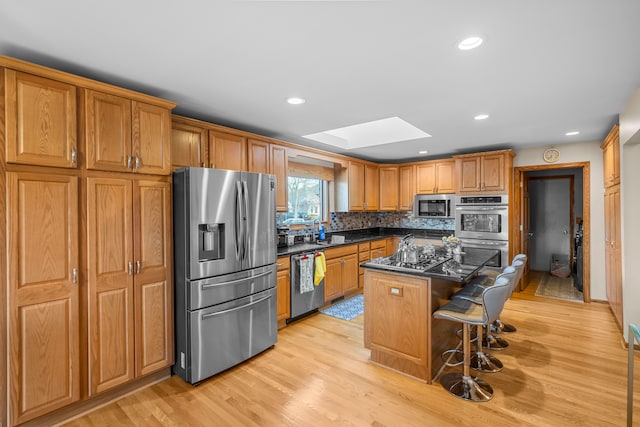 kitchen with a kitchen island, a skylight, a breakfast bar, stainless steel appliances, and light wood-style flooring
