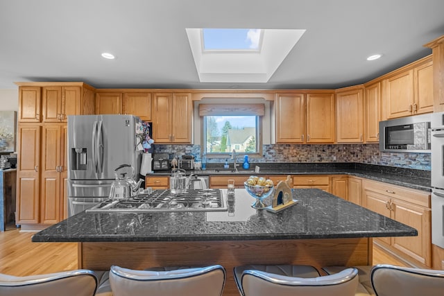 kitchen with a breakfast bar, a sink, a center island, stainless steel appliances, and a skylight