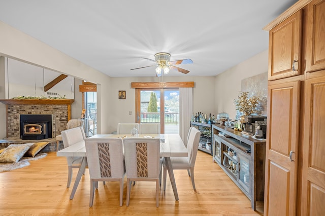 dining space featuring a ceiling fan, light wood-style flooring, and a brick fireplace
